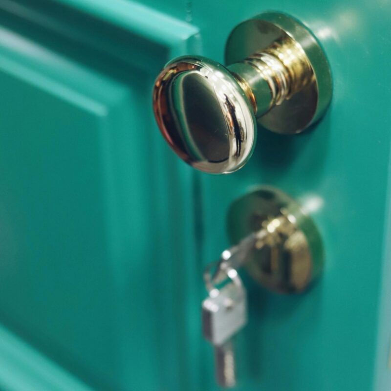 Close-up of a brass doorknob and key in the lock of a teal door.