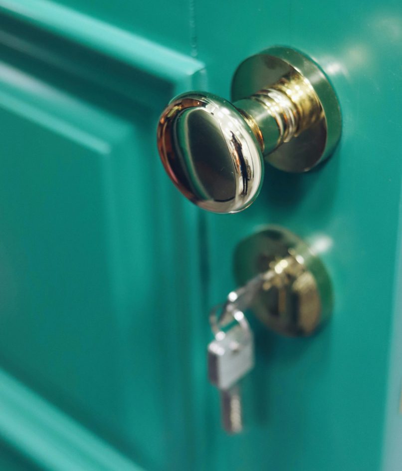 Close-up of a brass doorknob and key in the lock of a teal door.