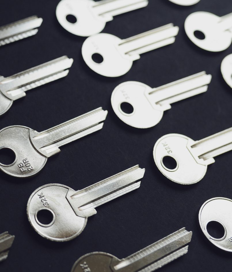 Close-up of multiple silver house keys arranged on a dark surface.